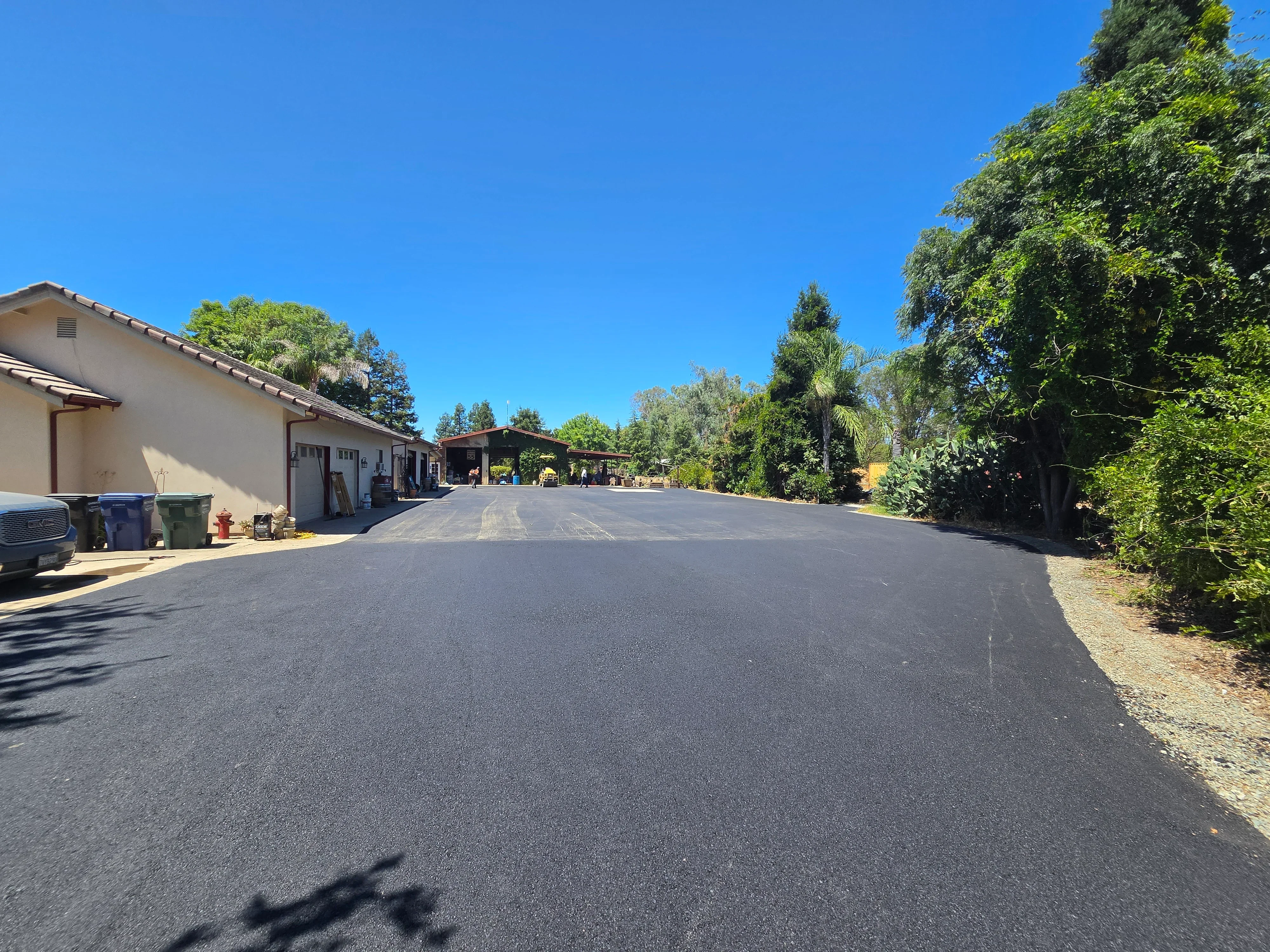 Newly paved asphalt driveway with smooth dark surface and gravel shoulders