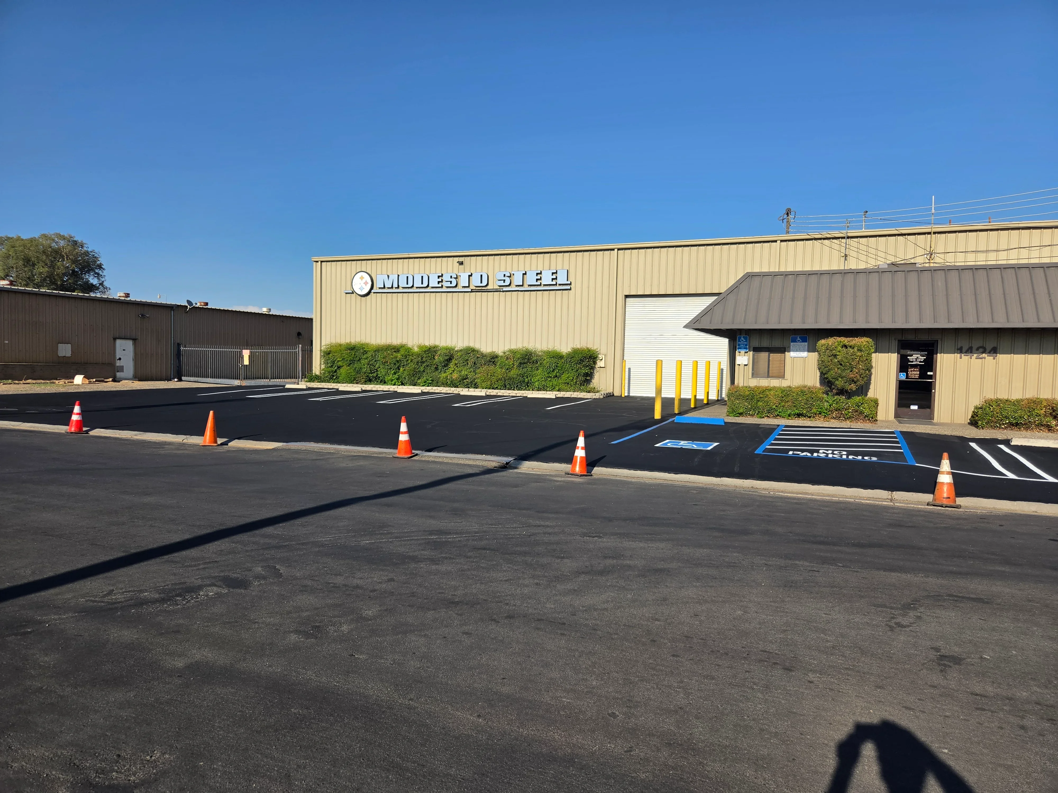 Newly paved asphalt parking lot with white striping and blue handicap spaces, traffic cones present